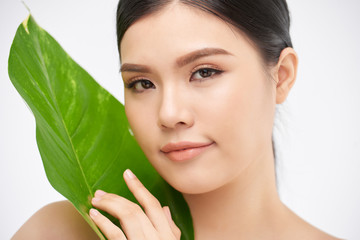 Young woman with clear skin touching green leaf and looking at camera on white background in studio