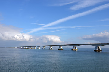Obraz premium Zeeland Bridge and Oosterschelde estuary in the Netherlands, under a predominantly blue sky with some comulus clouds approaching