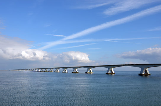 Zeeland Bridge and Oosterschelde estuary in the Netherlands, under a predominantly blue sky with some comulus clouds approaching