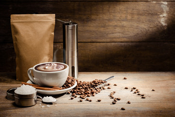 A Cup of latte art with paper bag of roasted coffee bean, sugar and cinnamon