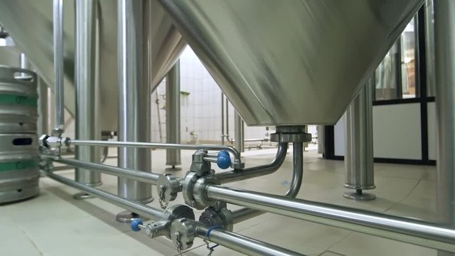 Low section tracking shot of modern brewhouse with system of steel vessels and canister connected with tubes