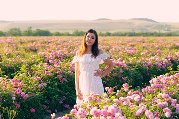 Beautiful young woman posing near roses in a garden.