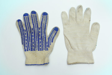 protective gloves of white fabric. intended for manual labor. with blue rubber dots on the working side and stretchable cuff with thin strip on hem. one of them lies face down. blue hue of background