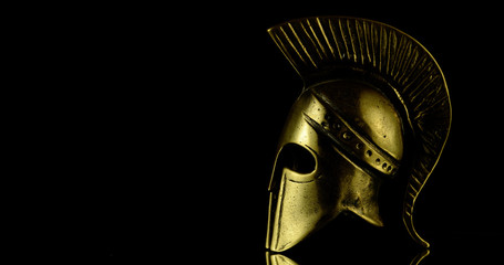 A wonderful golden spartan helmet as part of the equipment of ancient greek soldiers. King Leonidas and his 300th. The piece of metal stands against a black background
