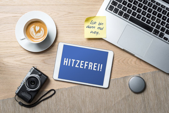 Hitzefrei written in german on tablet meaning having time off due to hot weather as flat lay from above on office desk