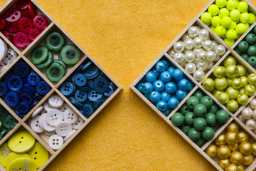 Clothes buttons in wooden box on yellow background. Closeup photo.