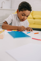 Naklejka premium portrait of african american boy drawing picture with colorful pencils at table in classroom