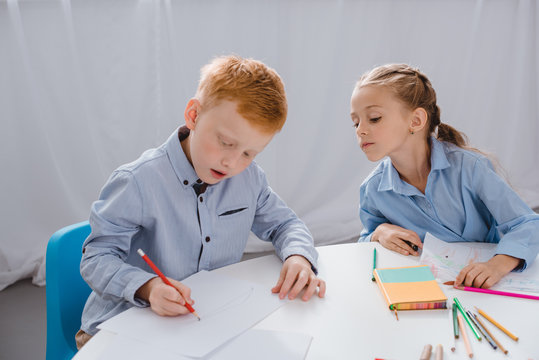 portrait of adorable kids drawing pictures at table in classroom