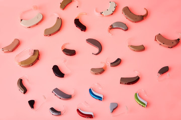 Different hearing aids on pink background, alternative to surgery. ENT accessory