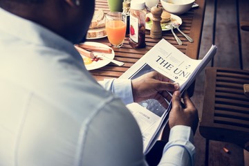 Rear view of black man reading newspaper while having breakfast