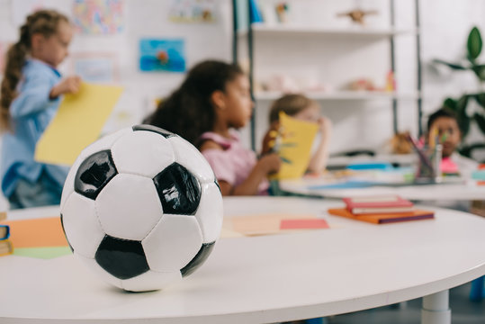 selective focus of soccer ball on table and multiracial preschoolers in classroom