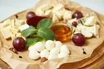 Maasdam, brie, camembert, roquefort cheeses on cheese board served with grapes, honey and sauce. Collection of  French and Italian cheeses on wooden board served with fruits. Isolated