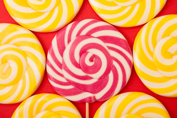 Sweet caramel candy on a red background. Bright lollipops. Yellow and pink sweets from the confectioner.