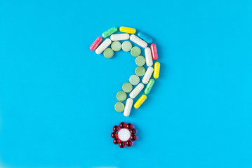 Question mark made of different colored pills, tablets and capsules on blue background. Pharmaceutical industry, and prescription minimal concept