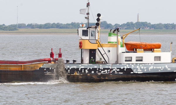 Sand dredging boat drawing away from coast shoreline to pump sand