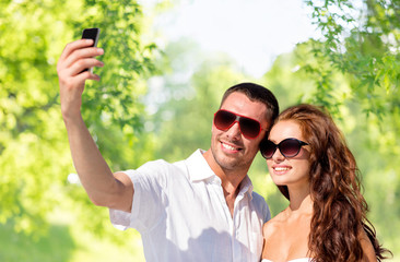 love, summer and technology concept - smiling couple in sunglasses making selfie by smartphone over green natural background