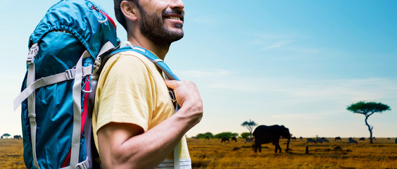adventure, travel, tourism, hike and people concept - close up of smiling man with backpack over animals in african savannah background