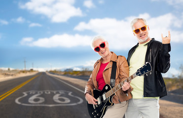 Obraz na płótnie Canvas rock music, old age and travel concept - happy senior couple with electric guitar over us route 66 background