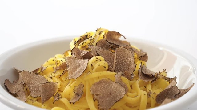 Fine grated black truffle falling on a plate of Italian fettuccine. Slow motion