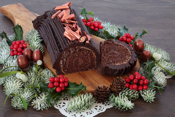 Chocolate yule log Christmas cake with winter flora of snow covered fir, holly, acorns and...