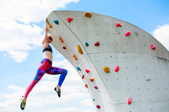 Photo of sporty woman in leggings hanging on wall for rock climbing against blue sky
