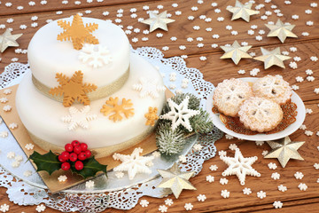 Iced Christmas cake with mince pies, snowflake decorations, gold stars, winter holly and fir on...