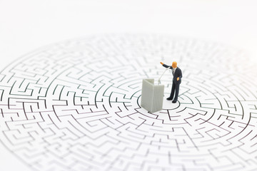 Miniature people: businessman stand with the podium on center of maze. Concepts of finding a solution, problem solving and challenge.