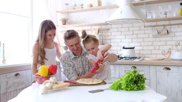 Father and daughters having a fun in the kitchen and making pizza