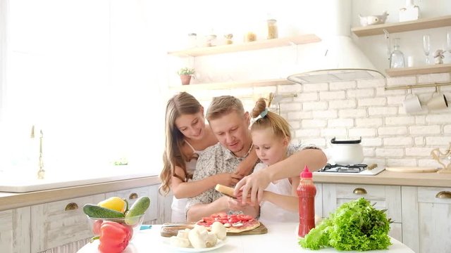 Father and daughters having a fun in the kitchen and making pizza