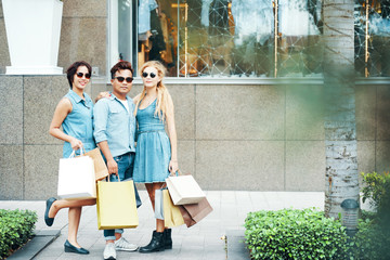 Cool man and women standing with paper shopping bags on street and looking at camera