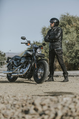 Man in black clothes posing close to his motorbike.