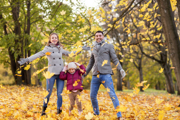 family, season and people concept - happy mother, father and little daughter playing with autumn...