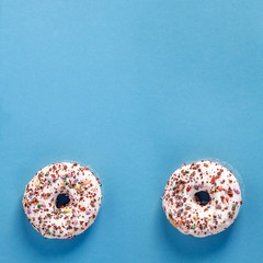 Two white donuts with colorful sprinkles on a blue blank background