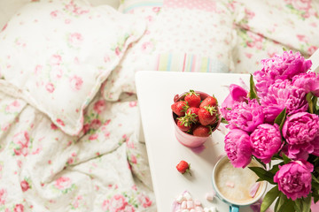 Gentle flowers are pink peonies, coffee with fluffy white milk foam and strawberries near the tender bed. The atmosphere of romance and pleasure.
