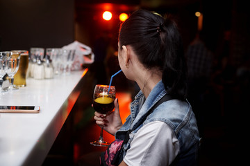 A girl with a cocktail sits for a bar counter.