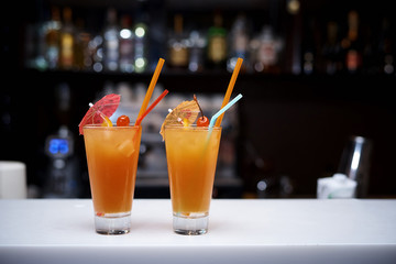 Cold orange cocktails with cherries, straws and umbrellas on the bar.