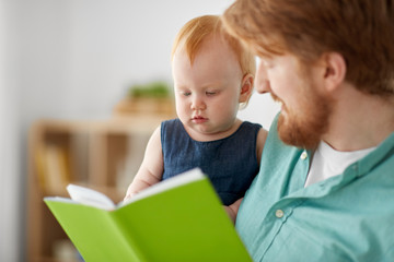 family, fatherhood and people concept - happy red haired father and little baby daughter with book at home