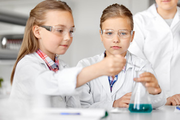 education, science, chemistry and children concept - kids or students with test tube making...