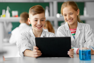 education, science and technology concept - kids with tablet pc computer studying chemistry at school laboratory