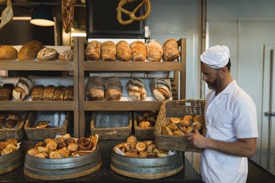 Male baker holding basket of croissants in bakery