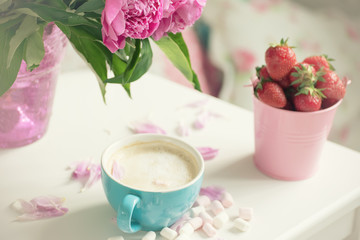 Fototapeta na wymiar Gentle flowers are pink peonies, coffee with fluffy white milk foam and strawberries. The atmosphere of romance and pleasure. 