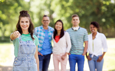 people, friendship and international concept - happy smiling woman pointing at you and group of happy friends outdoors