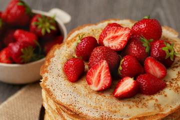 Thin pancakes with strawberries. A pile of thin freshly baked pancakes with strawberries. Sweet berries with pastries.