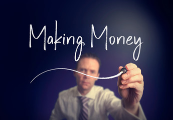 A businessman writing a make money concept with a white pen on a clear screen.