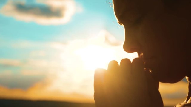 girl praying. girl folded her hands in prayer silhouette at sunset. slow motion video. Girl folded her hands in prayer pray to God. asks forgiveness for sins of repentance. believing lifestyle girl