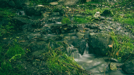 Small waterfall and creek surrounded with grey stones and green grass..Valle d'aosta, Italy.