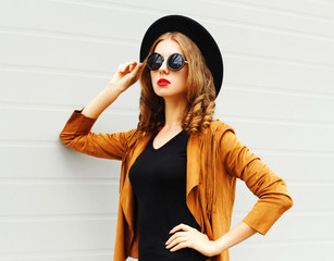 Beautiful woman model wearing a black hat, sunglasses and jacket looking in profile over urban grey background