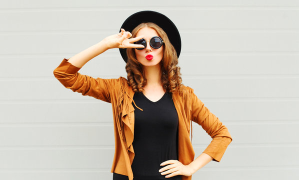 Cool girl wearing a black hat, sunglasses and jacket having fun over urban grey background