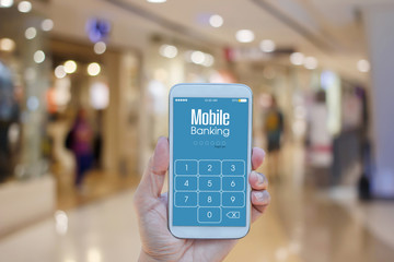 Hand holding smartphone with Mobile Banking on screen over blurred in shopping mall background