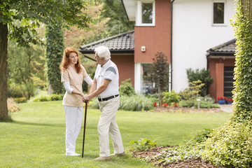 Smiling caregiver supporting senior man with walking stick in the garden